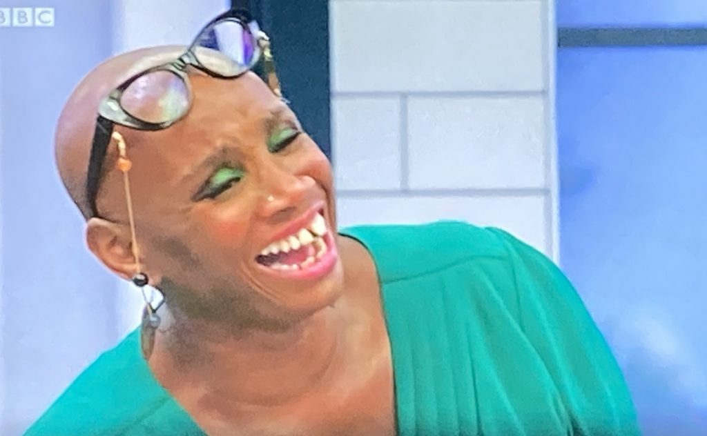 Andi Oliver, with glasses perched on her head, laughing, wearing a green blouse and matching eye shadow